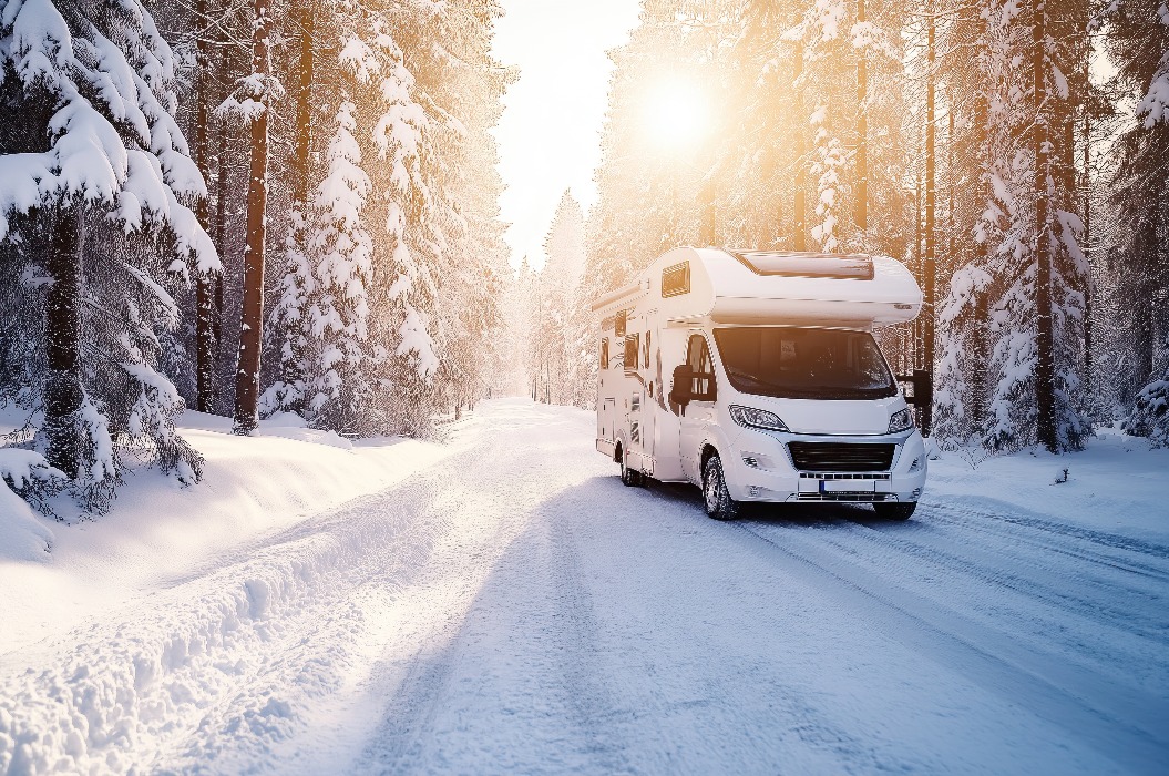 Weißes Wohnmobil auf schneebedeckter Straße im Winterwald