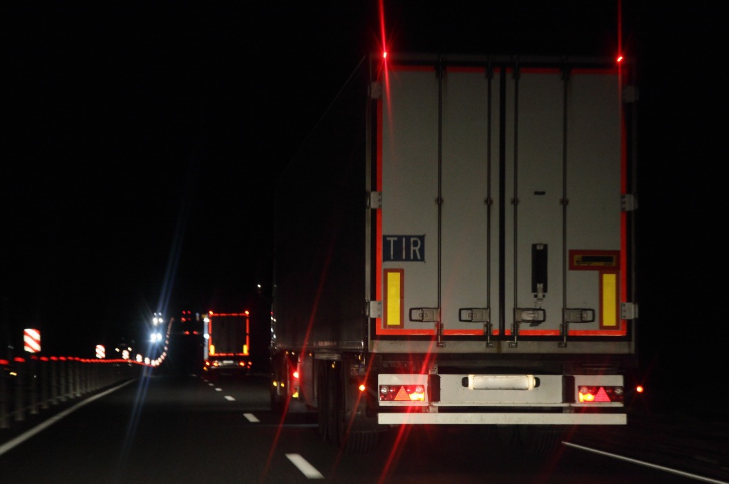 Sattelschlepper mit Beleuchtungsreflexionsstreifen fahren auf trockener asphaltierter Nachtstraße im Dunkeln, Rückansicht.