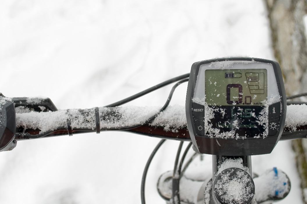 Detailaufnahme des Lenkers und des Displays eines Elektrofahrrads, E-Bike, E-Bike, verschneiter Bergwald während eines Schneesturms, Blizzard, Sport, Ende des Winters, Kälte, Alpen, Abenteuer, Piemont, Italien